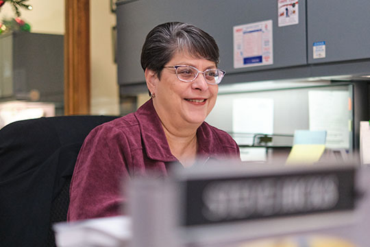 Agent Patti Gorentz smiles as she looks over her desk to assist a customer at Dittmann Insurance Agency in Pittsburg, Kansas.